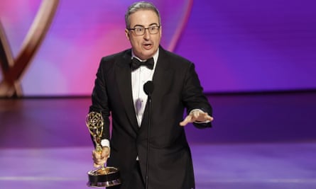 man wearing black suit and black bowtie holds gold statue