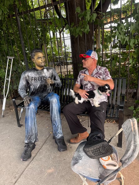 a man sits on a bench next to a lifesize statue of Charlie Kirk