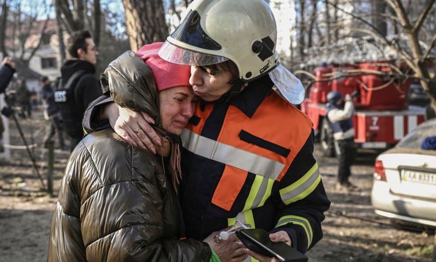 An evacuated resident is comforted by rescue staff outside a burning apartment building in Kyiv, Ukraine.