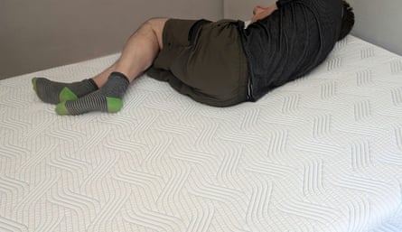 The reviewer’s husband, shoeless, lies on the Tempur Pro Plus SmartCool mattress, which is on a base but which has no bedding.