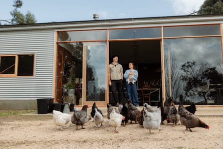 A man and woman, holding a baby, in the doorway of a shed, with chickens in front
