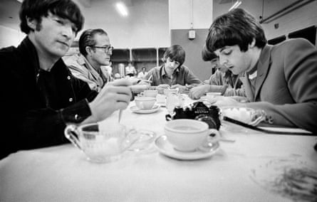 The Beatles and Gleason sitting at a long table covered with a white tablecloth, doodling and drinking tea