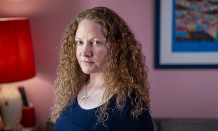 Imogen May inside her house with a pink wall and picture frame and lamp behind her.