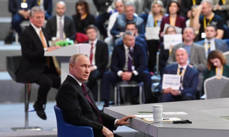 Putin sits at a table as audience members look on