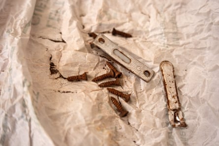 On a crumpled piece of white paper are eight rusted screws and a pair of nail clippers, broken in half and covered in rust spots.