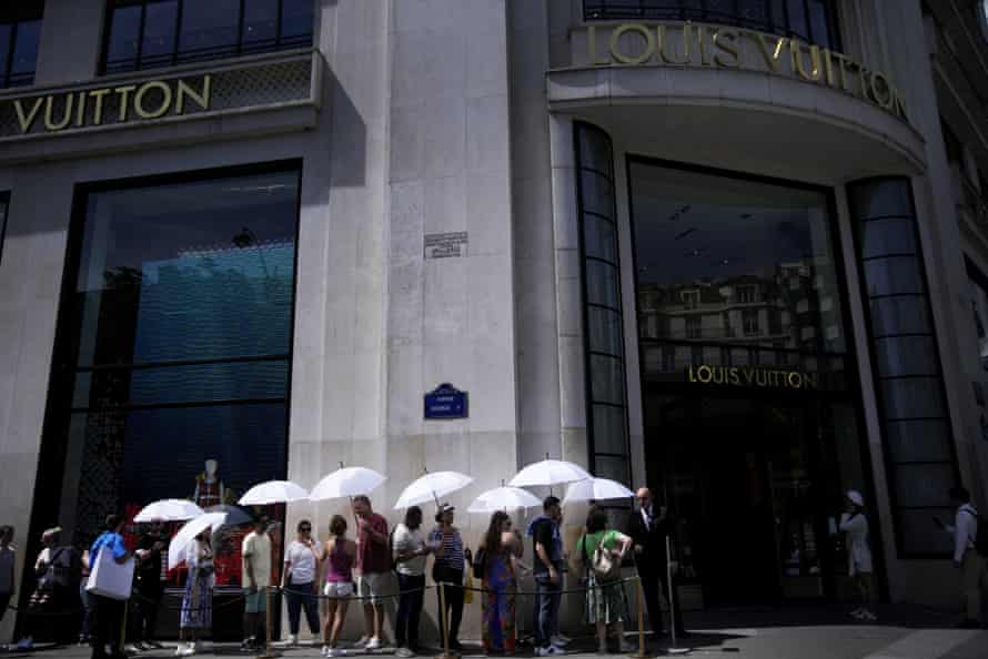 People use umbrellas to protect from the sun as they queue to enter the Louis Vuiton store on the Champs Elysee avenue, in Paris, France