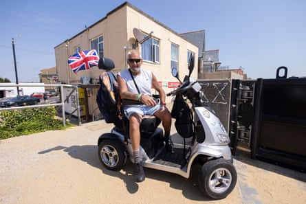 Chris sitting on a mobility scooter flying a union flag on a beach walkway