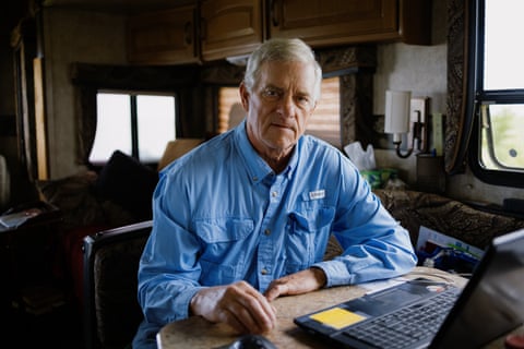 A middle-aged man in a blue button-up shirt sits in front of a laptop.