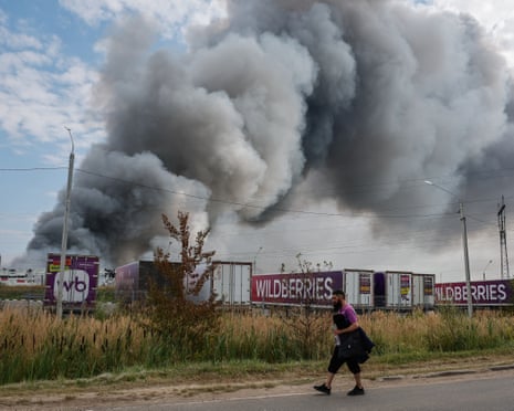 A man walks past a large plume of grey smoke rising from a warehouse