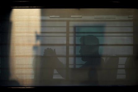 A man sits on a bus behind tinted and barred windows