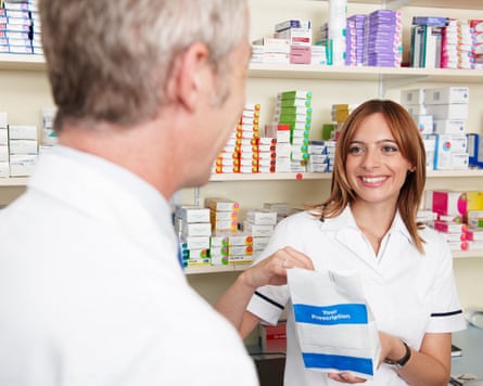 a pharmacist worker hands a bag of prescription items to a customer