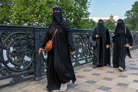 Three women wearing black niqabs walking along a bridge