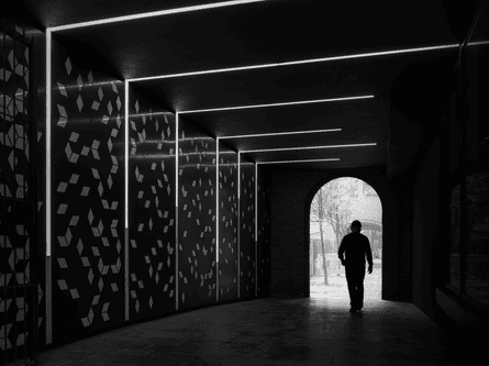 A black and white shot of a person walking into a dark tunnel with lights and patterns on the walls
