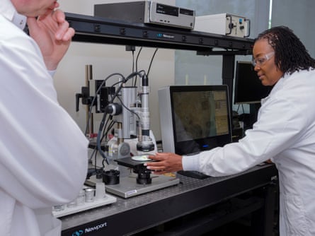 Two people in scrubs look at a microscope.