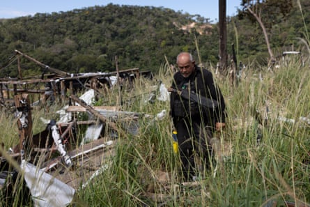 Nilton Tubino walks through long grass next to the wreckage of buildings