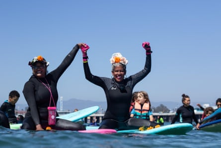 Two people smile while holding hands and cheer while sitting on their boards in the water