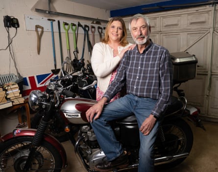 David Osenton sits on a Triumph motorbike in a garage with Karen beside him