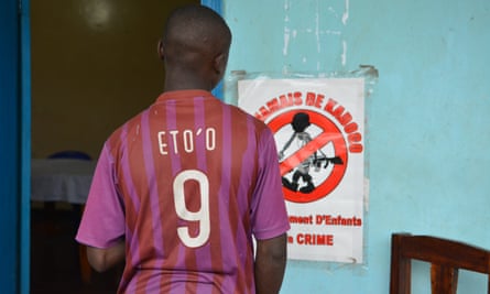 A boy wearing a Samuel Eto’o number 9 football shirt stands with his back to the camera looking at a small poster on a wall.