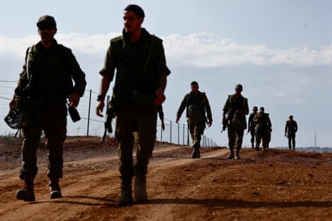 A group of soldiers, walking two abreast along the length of a long fence