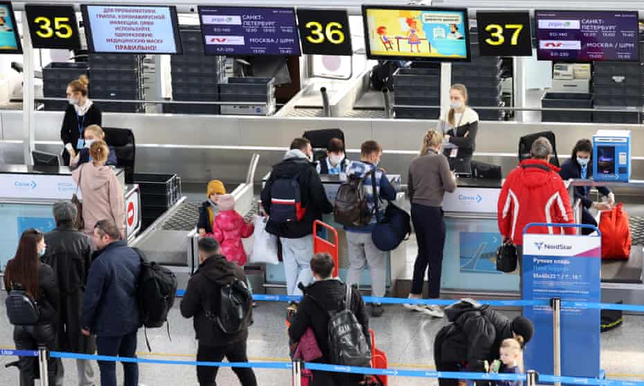 Passengers pulling suitcases and wearing backpacks wait in line by check-in desks at Sochi International Airport.