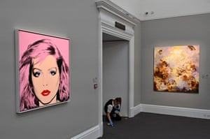 London, UK. An employee at Sotheby's cleans the floor near an artwork by Andy Warhol entitled Debbie Harry