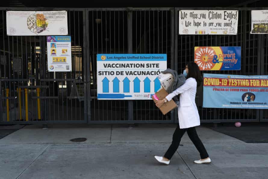 woman carries box in front of signs saying los angeles unified school district vaccination site