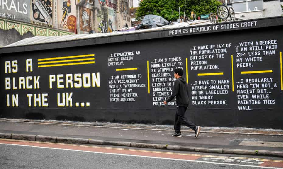 A man walks past street art by Lanie Rose and @asablackpersonintheuk in Stokes Croft, Bristol.