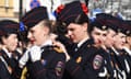 A line of female military cadets. Nearest the camera, one applies red lipstick to the cadet next to her