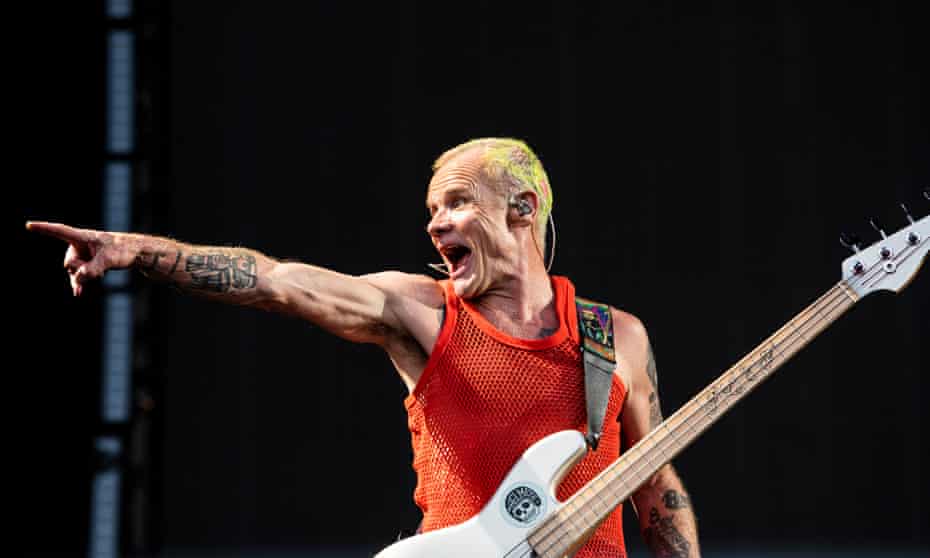 Flea of Red Hot Chili Peppers on stage, in red net vest with yellow bleached short hair