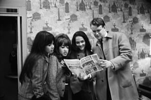 Three women look at a magazine being held by a man