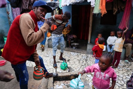 A man brushes his teeth in a yard with five small children and a few adults in the background