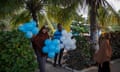 A woman and man smile as they carry blue and white balloons along a path in a park