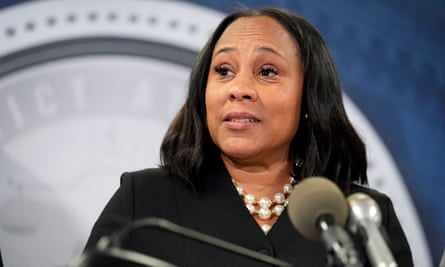 Middle-aged Black woman, shoulder-length black hair, black suit, big white pearls, speaks at lectern.