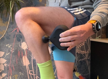 The writer wearing training gear holding a massage gun to his left calf