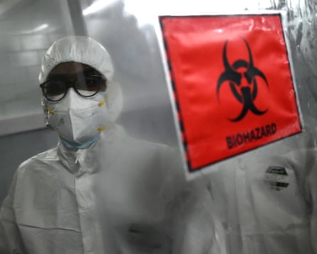 Technicians wearing hamzat suits stand behind a biohazard sign inside a molecular laboratory facility set up to test for monkeypox