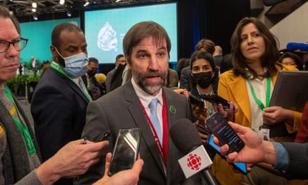 A bearded white man in a suit speaks to journalists in a conference hall