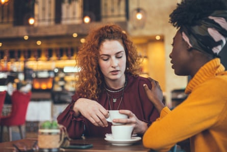 Two women having coffee in a bar, one woman appearing to be supportive of the other, who is looking rather down
