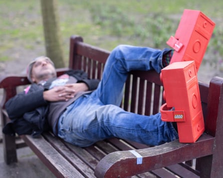 Rich Pelley lying on a park bench wearing Lego Crocs