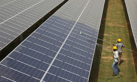 Workers clean photovoltaic panels at a solar power plant in Gujarat, India