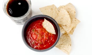 Close-Up Of Salsa Dip With Tortilla Chips And Soda Against White BackgroundOverhead closeup shot of a black bowl filled with salsa with tortilla chips laying next to it with one in the bowl and a glass of soda at the top left of the frame against a white background (Overhead closeup shot of a black bowl filled with salsa wit