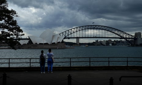 Tourists taking photos of the Sydney opera house and harbour bridge on a dark and cloudy day