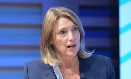 Woman wearing a blue suit against a blue background, talks to someone off-camera.