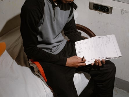 A boy sits on a bed holding a notebook with tally marks on it