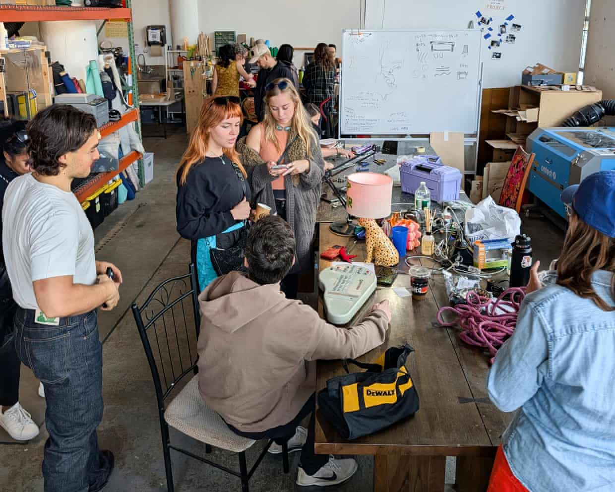 Group of people gather around a cluttered workbench examining tools and electronics