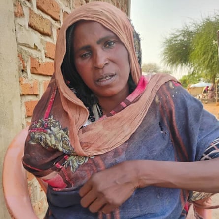 An African woman with an eye missing and an empty sleeve sits outside a brick building