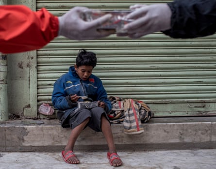Hands wearing protective gloves exchange a container of food in front of a child who is eating from a similar container
