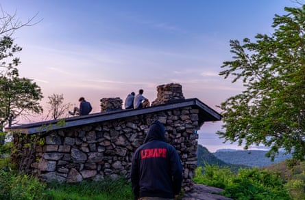 A person wearing a sweatshirt with Lenape on it, people in the background sitting on a roof