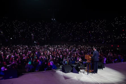 a man stands on stage as an arena full of people hold up flashlights