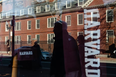 A redbrick building’s reflection against a window with Harvard in white letters and all caps