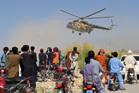 Residents watch a Pakistani army helicopter preparing to land with a rescue team following an earthquake in the remote mountainous district of Harnai.